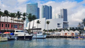 A marina with boats docked, a modern building with a curved facade, and palm trees. - YOTEL Miami (Miami)