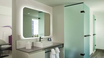 A modern bathroom with a large mirror, two sinks, and a glass door closet.