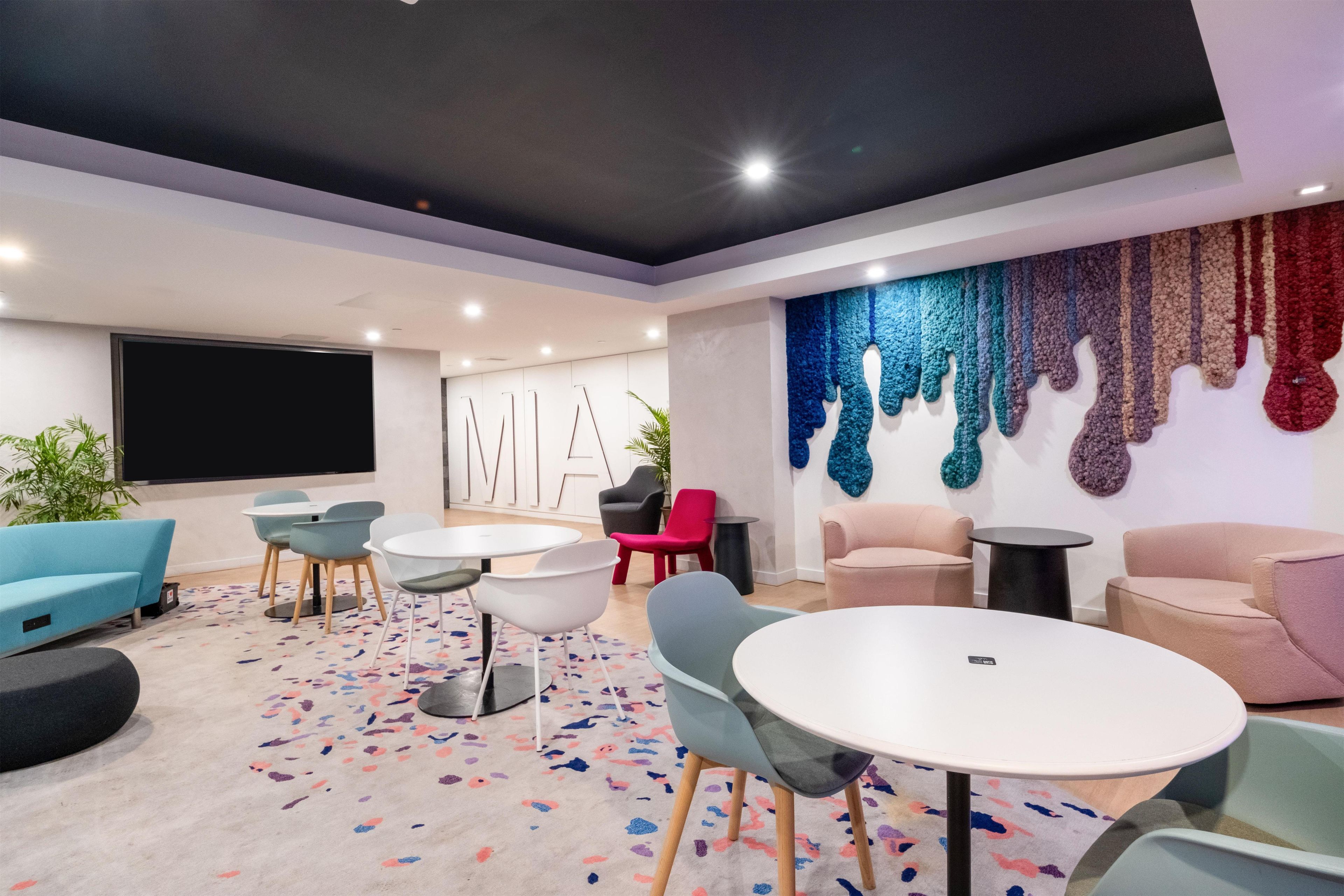 A modern conference room with round tables, chairs, and a large screen.