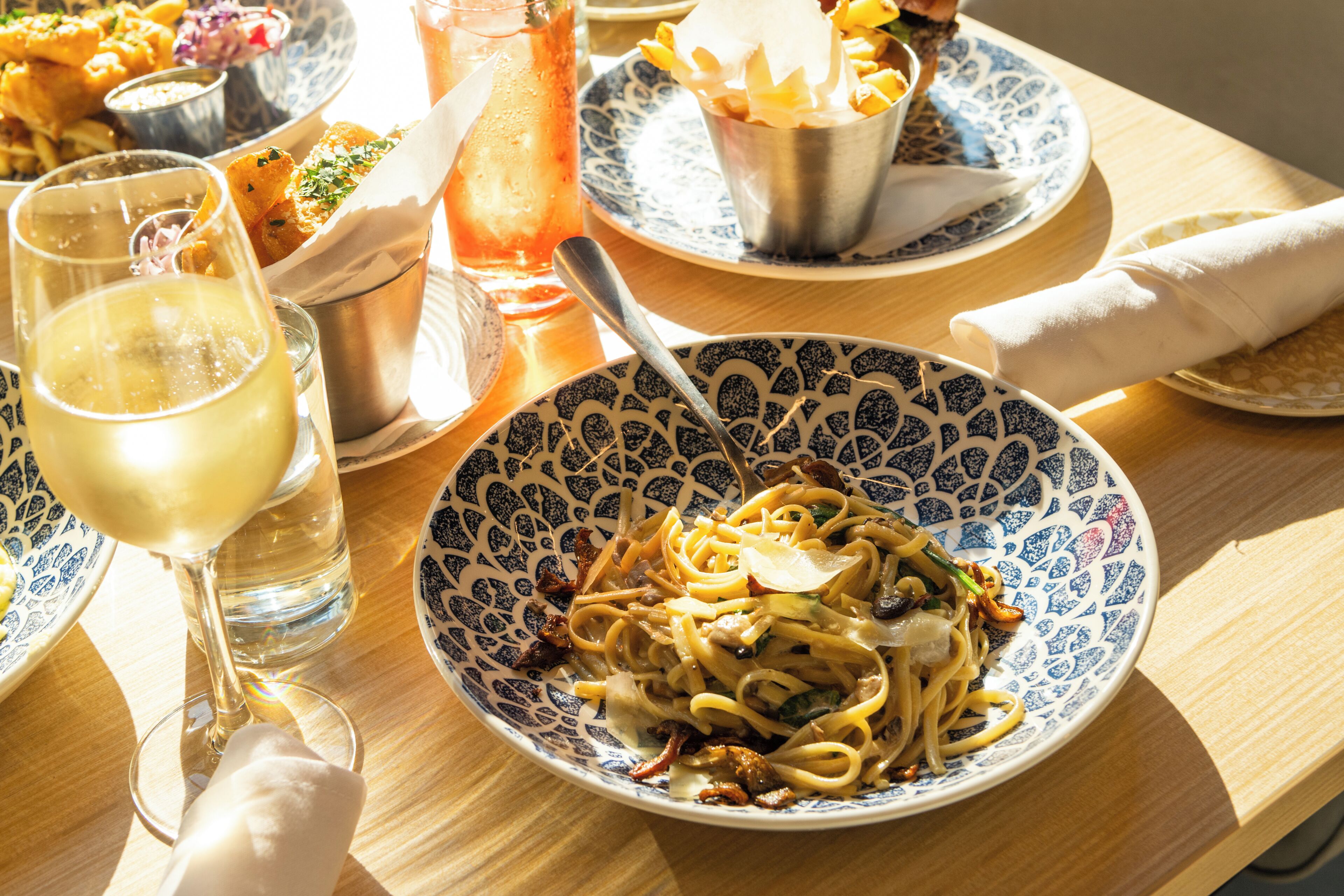A dining table with a plate of pasta, a glass of wine, and a pitcher of iced tea.