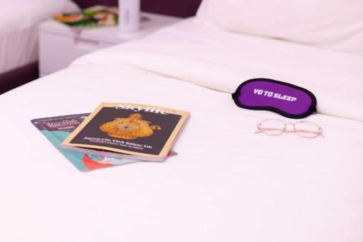 A hotel room with a bed, pillows, a bedside table with a lamp, and a book.