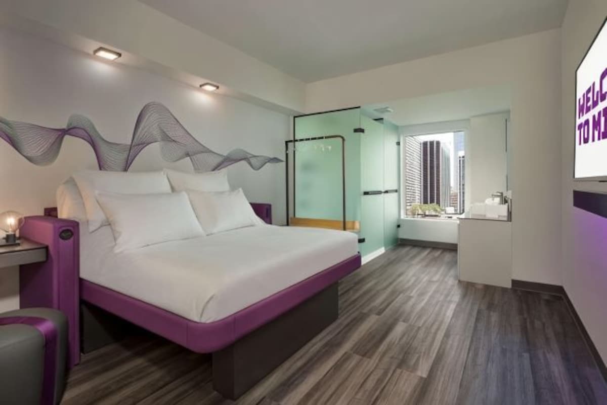 A modern hotel room with a large bed, a desk, and a view of the city.