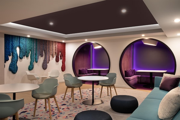 A modern interior with a round table, chairs, a sofa, and a wall with textured art.