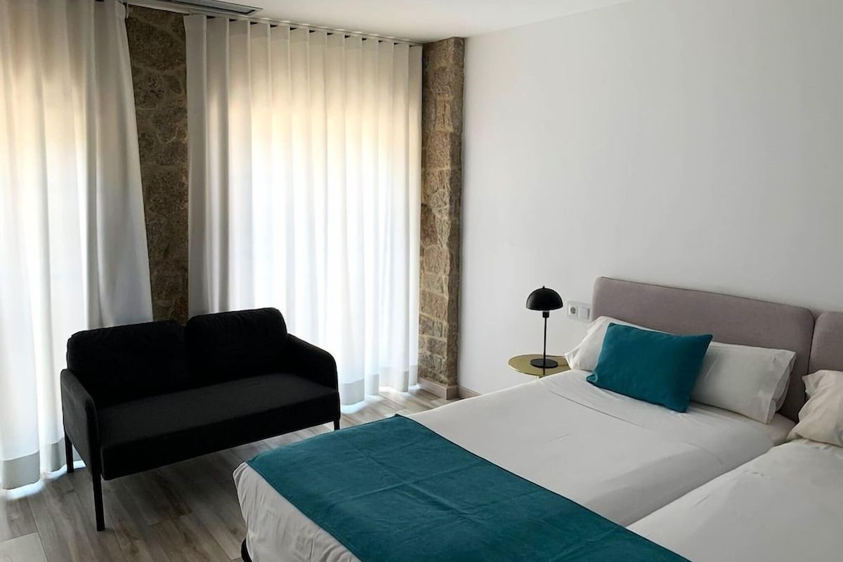 Une chambre d’hôtel avec un lit, un canapé, une table de chevet et une fenêtre avec des rideaux.
