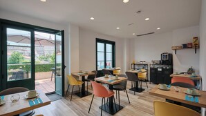 A modern dining area with multiple tables and chairs, a coffee machine, and a view of the cityscape through large windows. - Pombal Rooms (Santiago de Compostela)