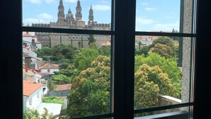 A view through a window with a balcony, featuring a historic building with two towers in the background. - Pombal Rooms (Santiago de Compostela)