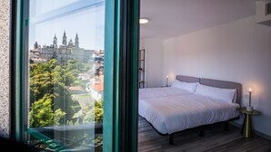 A bedroom with a large window, a bed, bedside tables, and a view of a cityscape. - Pombal Rooms (Santiago de Compostela)