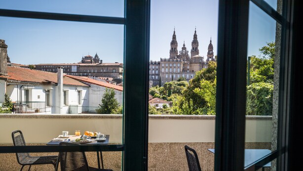 A balcony with a table set for breakfast, overlooking a historic building with two prominent towers. - Pombal Rooms (Santiago de Compostela)
