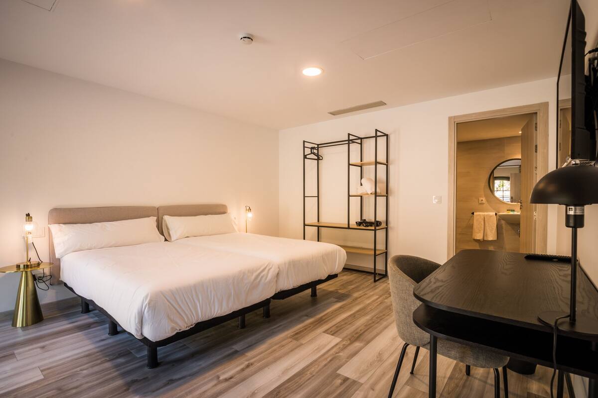 Ein Hotelzimmer mit Bett, Nachttisch, Lampe und Schreibtisch mit Stuhl.