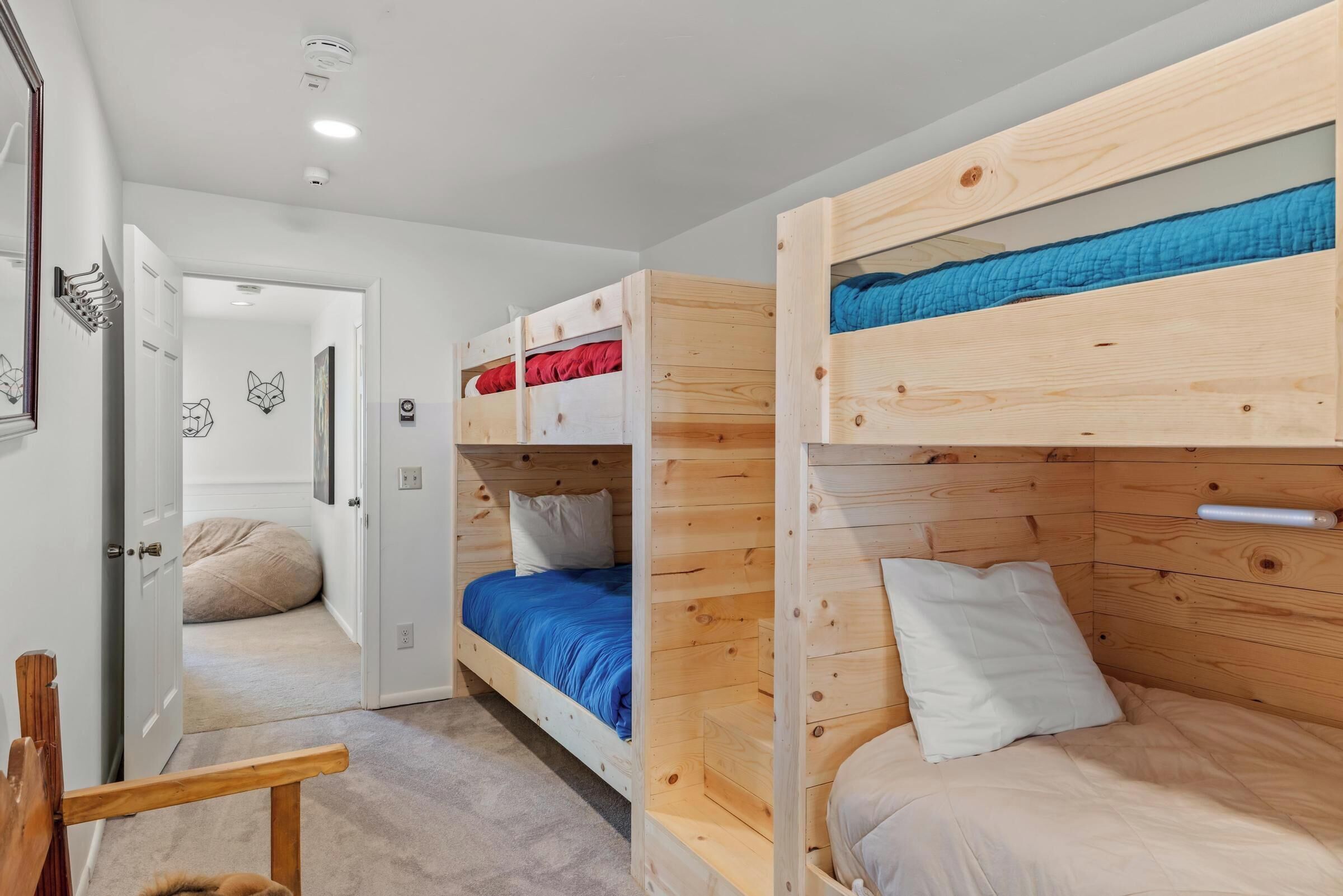 Une pièce avec des lits superposés, une porte donnant sur une autre pièce et une petite chaise en bois.