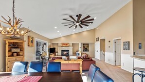 Uma sala de estar espaçosa com uma mesa de jantar, cadeiras azuis, lareira e ventilador de teto.