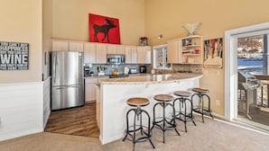 Uma cozinha moderna com ilha central, banquetas, eletrodomésticos de aço inoxidável e uma grande janela com vista.