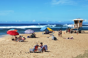 Une plage avec des parasols, des chaises longues et un poste de surveillance pour les sauveteurs.