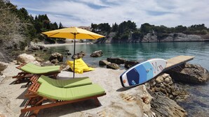 Ein Strand mit Liegestühlen, einem gelben Sonnenschirm und einem Surfbrett.
