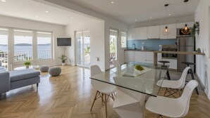 Eine moderne Küche mit weißen Schränken, einem Edelstahlkühlschrank und einem Glastisch mit weißen Stühlen.