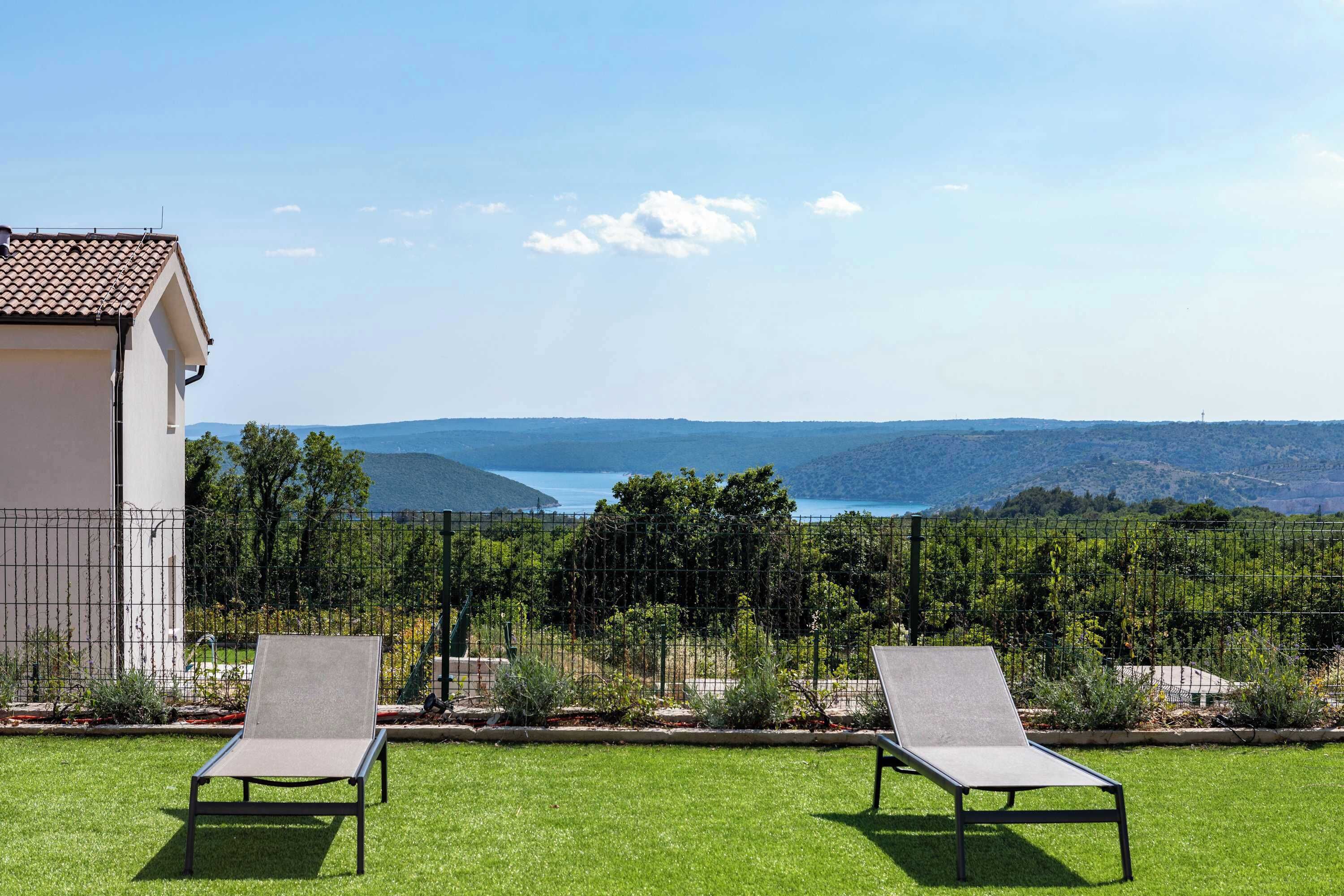 Dos sillones de jardín sobre un césped con vistas a un cuerpo de agua y colinas.