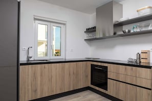 A modern kitchen with wooden cabinets, a black countertop, and a built-in dishwasher. - Villa Lumina (Sveti Lovrec Labinski)