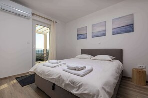 Un dormitorio con una cama, una mesita de noche de madera, aire acondicionado en la pared y vistas al exterior.