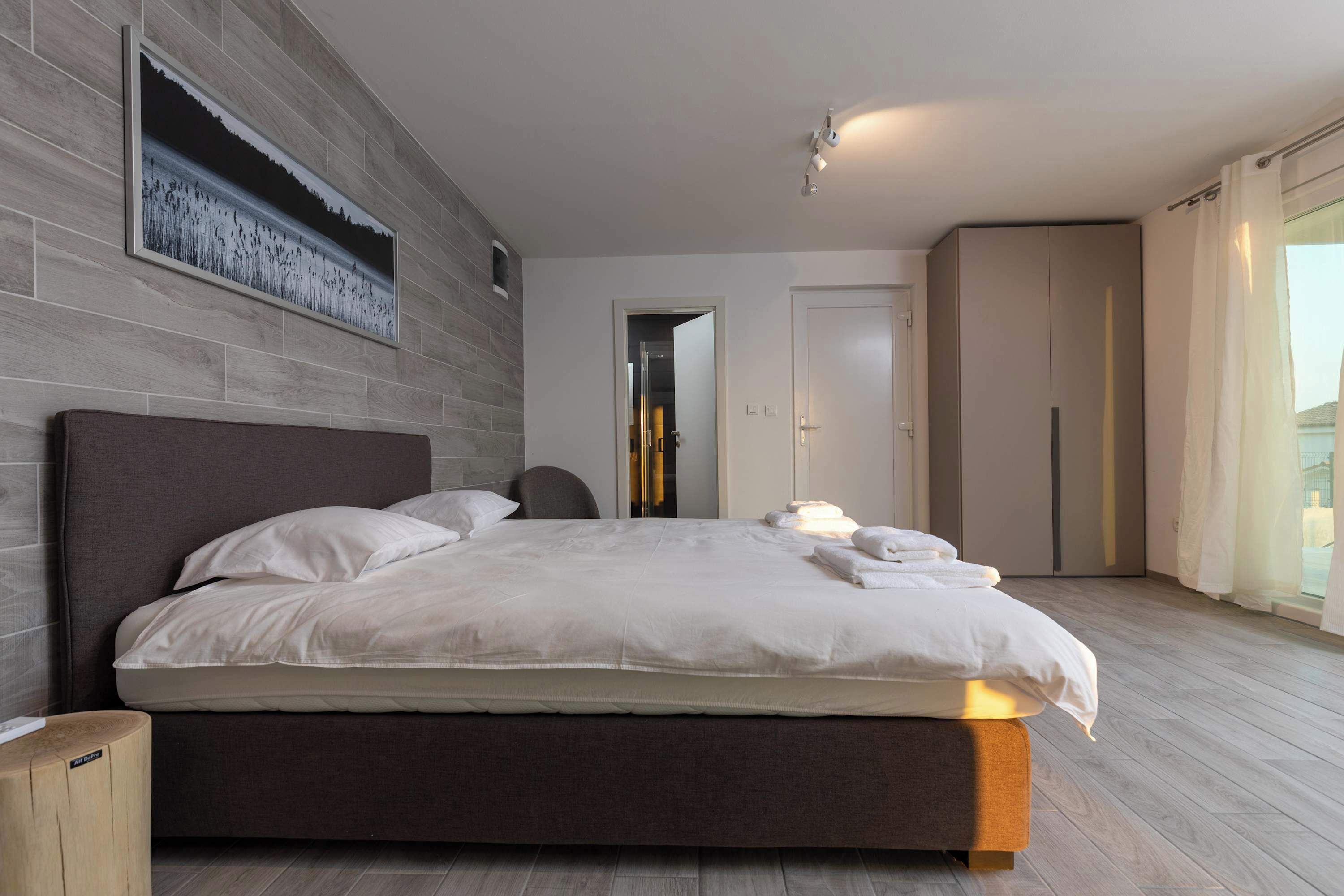 Ein modernes Schlafzimmer mit einem großen Bett, einem Kopfteil, einem Nachttisch und einem an der Wand befestigten Kunstwerk.