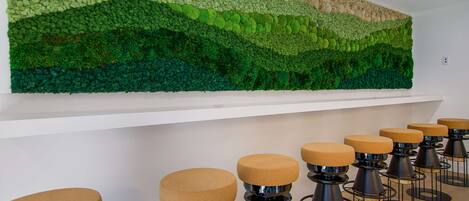 A room with a wall-mounted green moss art piece and a row of stools with round tops.