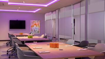 A modern conference room with a long table, chairs, a flat-screen TV, and glass walls.