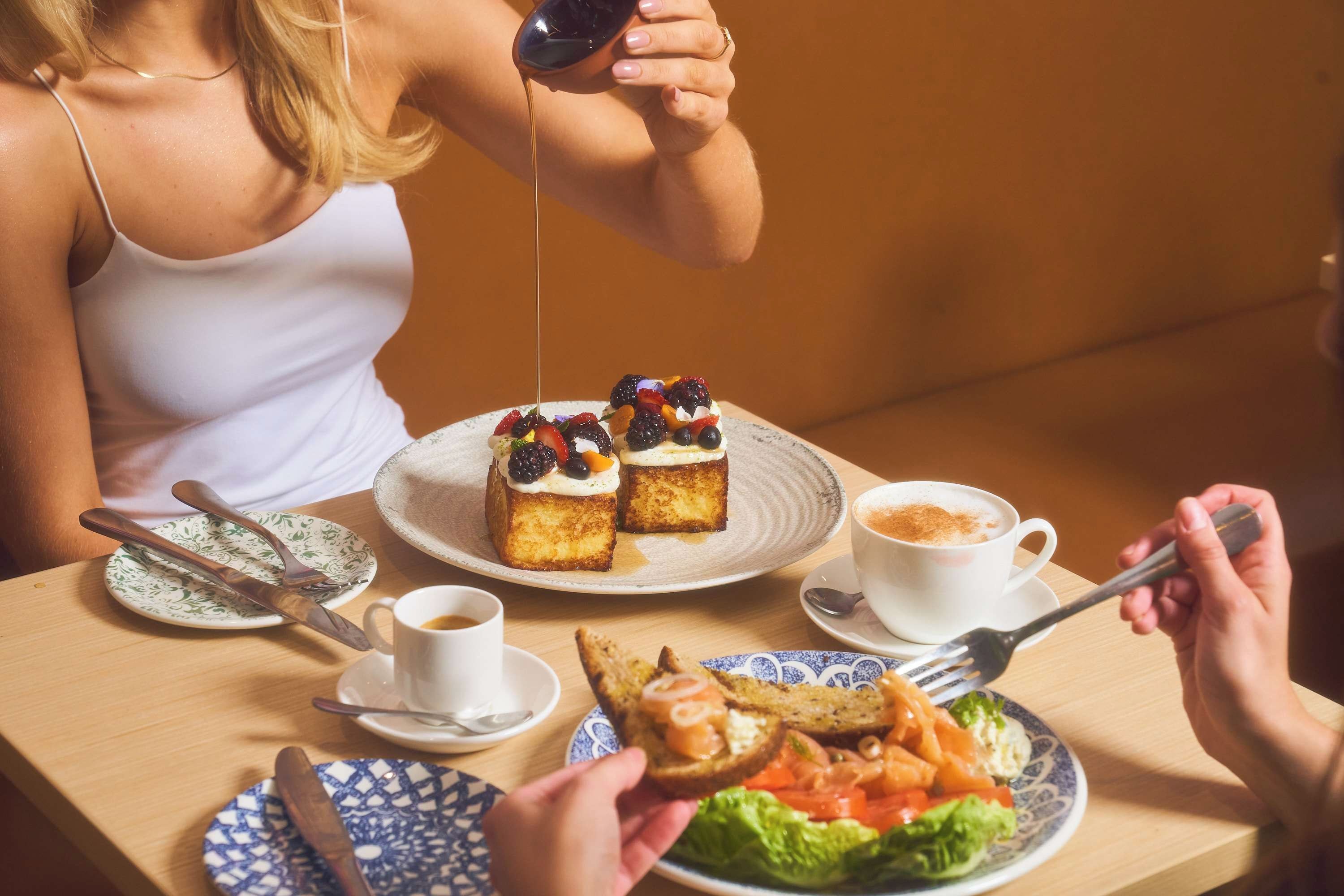 A dining table with a plate of toast topped with berries and cream, a cup of coffee, and a plate of salad.