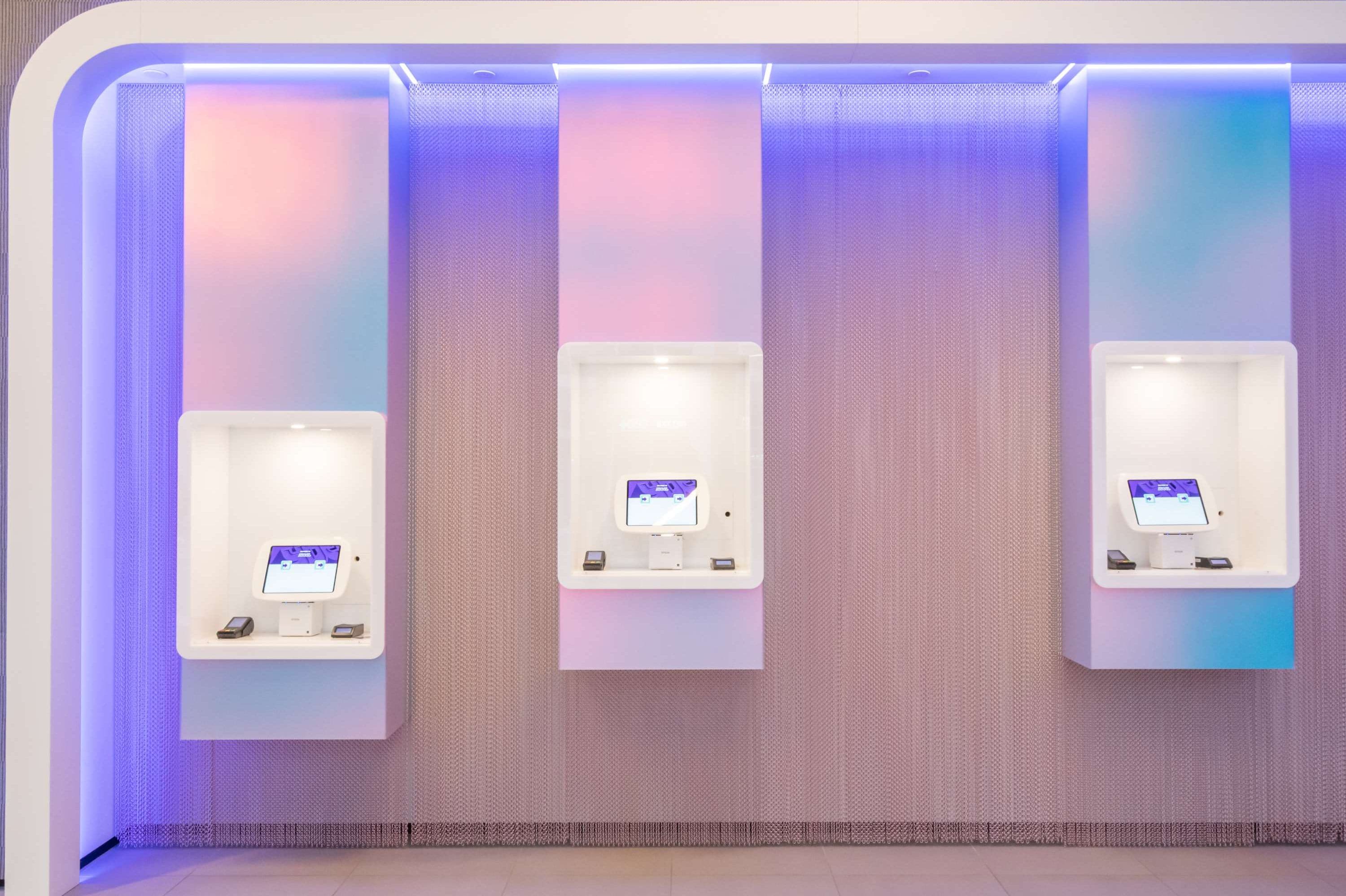 Three self-service kiosks with screens, mounted on a wall with a textured finish.