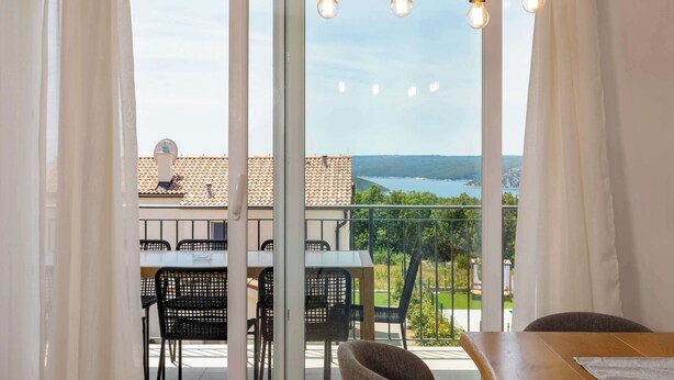 Ein Balkon mit Tisch und Stühlen, Blick auf einen See und ein Gebäude mit Ziegeldach.