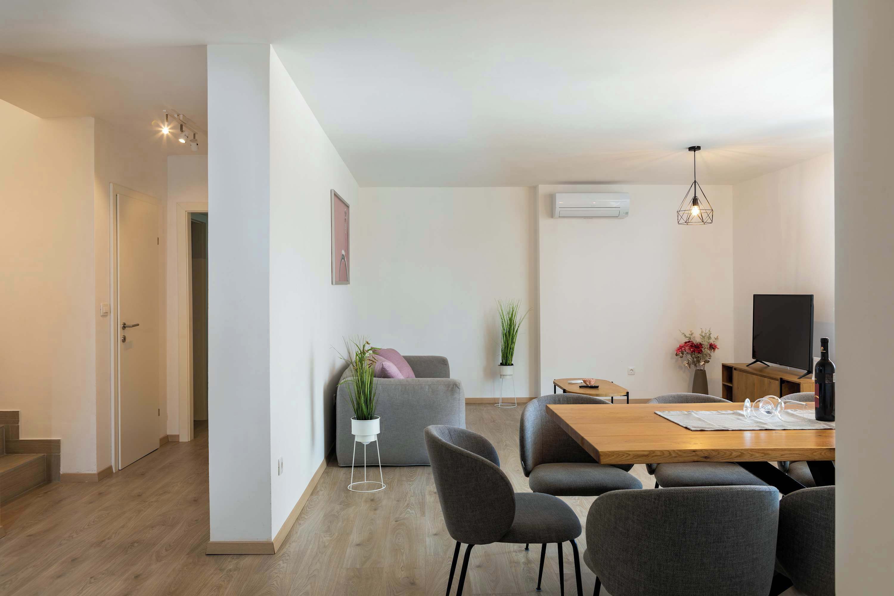 Un espacio de estar moderno con zona de comedor, sofá gris y una escalera.