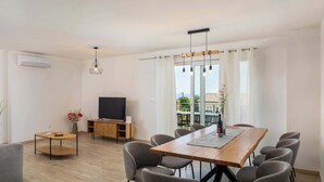 Ein modernes Wohnzimmer mit Essbereich, einem Flachbildfernseher und einem großen Fenster mit Vorhängen.