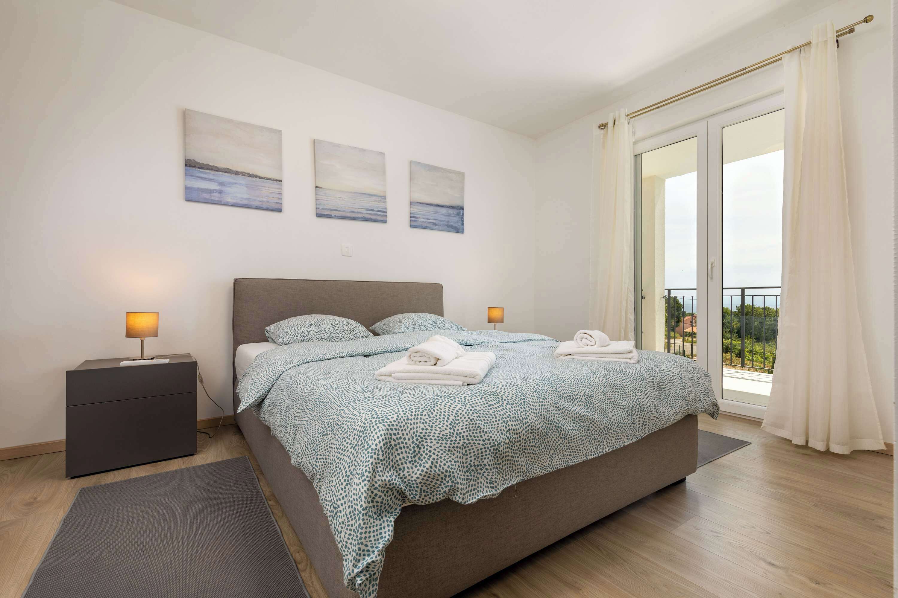 A bedroom with a bed, nightstands, a view through a glass door, and artwork on the wall.