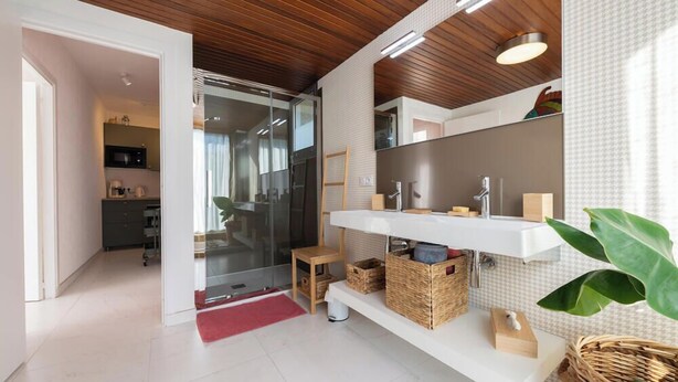A modern bathroom with a white vanity, a large mirror, and wicker baskets. - Elégant T2, 4⭐, cadre verdoyant, centre ville 750 m, plage et GR34 à 3 km. (Fouesnant)