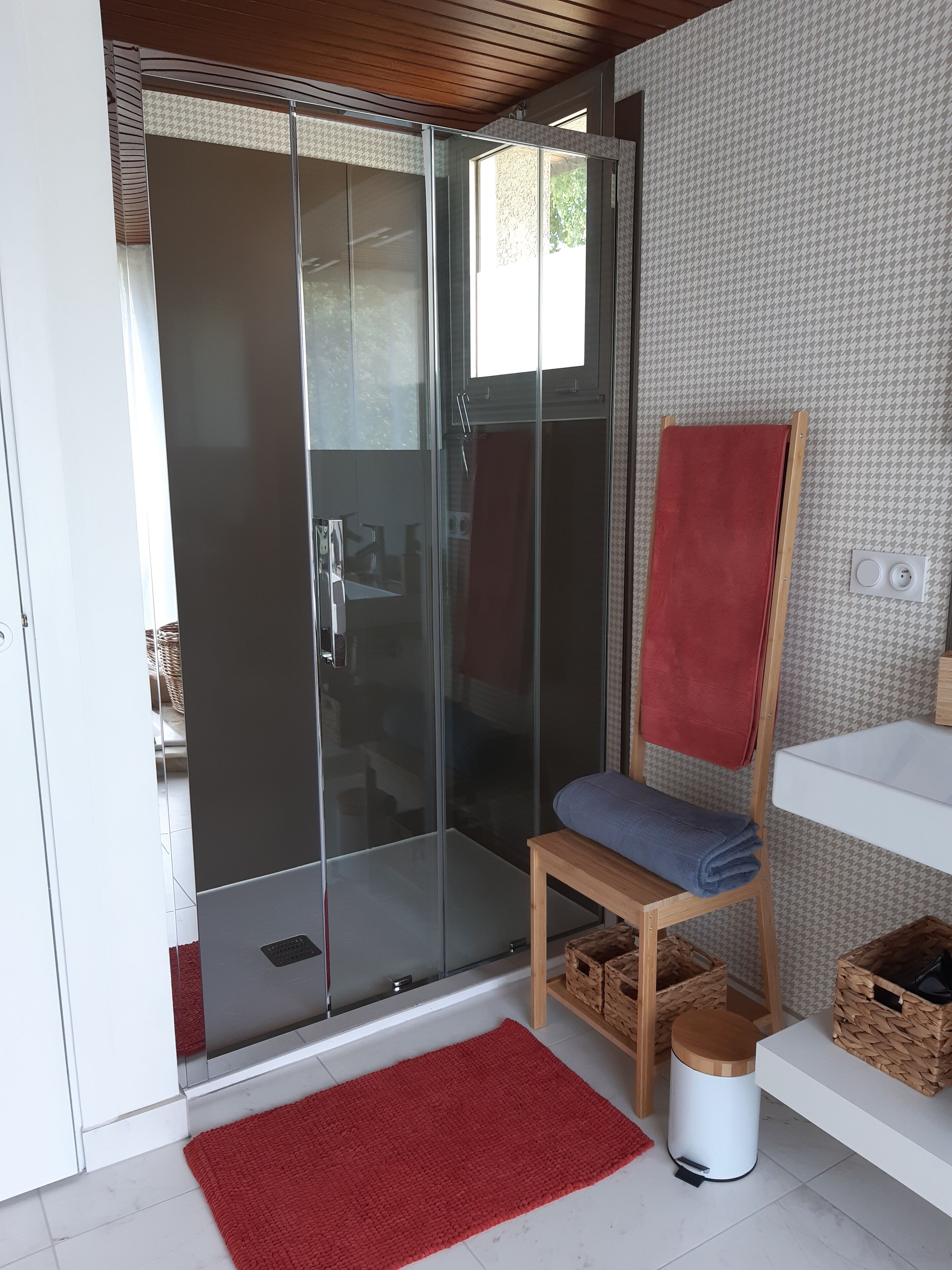Ein modernes Badezimmer mit einer Duschkabine aus Glas, einer Holzbank mit Handtüchern und einem weißen Waschbecken.