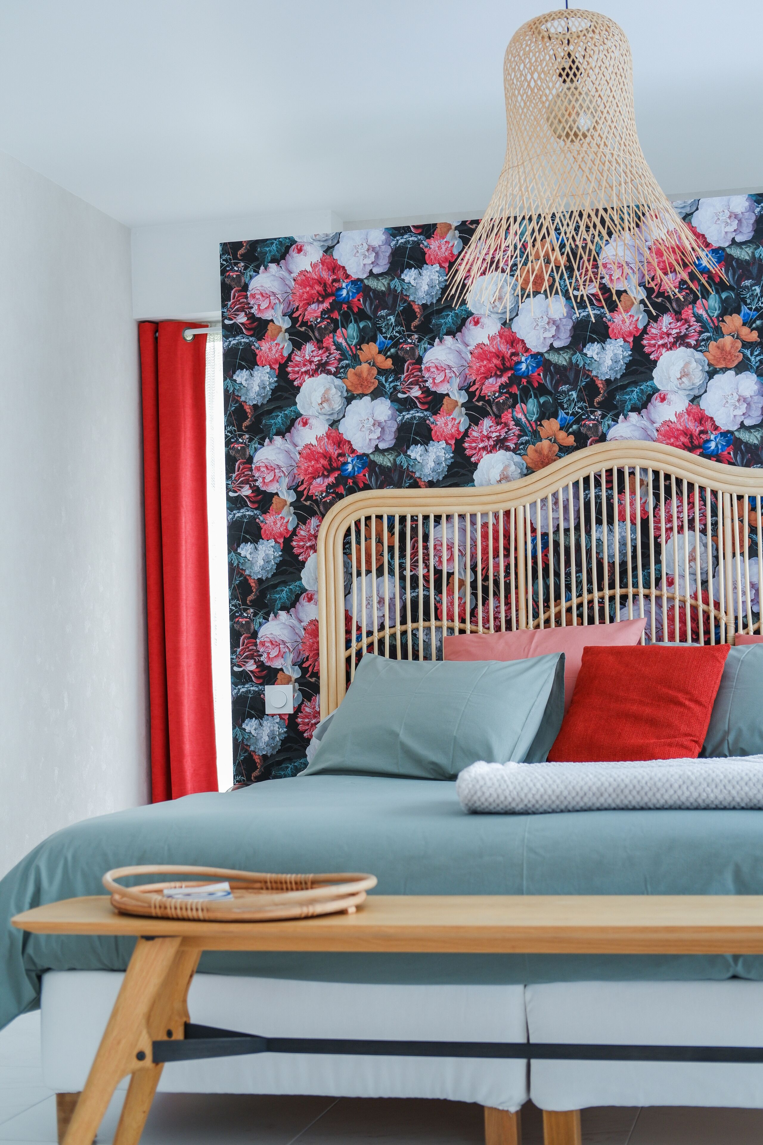 A bed with a wooden headboard, a woven hanging light fixture, and a floral-patterned wall.