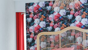 A bed with a wooden headboard, a woven hanging light fixture, and a floral-patterned wall. - Elégant T2, 4⭐, cadre verdoyant, centre ville 750 m, plage et GR34 à 3 km. (Fouesnant)