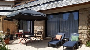 An outdoor patio with a table and chairs, a lounge area with two chairs, and a large umbrella. - Elégant T2, 4⭐, cadre verdoyant, centre ville 750 m, plage et GR34 à 3 km. (Fouesnant)