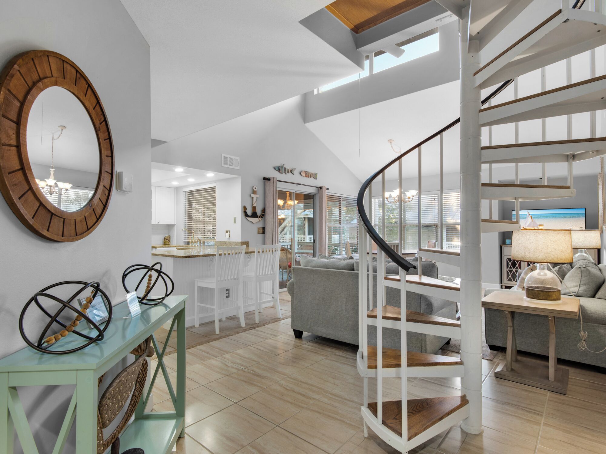 A spacious living area with a curved staircase, a kitchen with a view, and a large mirror on the wall.