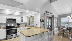 A modern kitchen with white cabinetry, stainless steel appliances, a granite countertop, and a dining area with a table and chairs. - Cottage 187, Spacious, Closest Cottages to the Beach, Free Beach Chair Service (Miramar Beach)