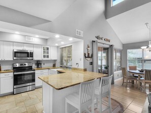 Enjoy cooking in this well-equipped kitchen with stainless steel appliances, a granite countertop island, and a dining area with a table and chairs.