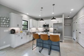 A modern kitchen with white cabinets, a central island with bar stools, stainless steel appliances, and pendant lighting.