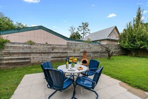 Une terrasse avec une table ronde et des chaises bleues, une clôture en bois et, au fond, un bâtiment doté d’un toit végétalisé.