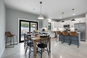 Une cuisine moderne avec des meubles blancs, des appareils en acier inoxydable et un coin repas comprenant une table et des chaises en bois.