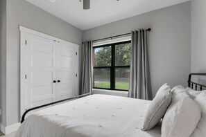Une chambre à coucher avec un grand lit, une fenêtre avec des rideaux, une armoire blanche et un ventilateur de plafond.
