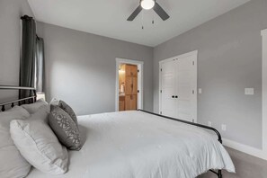 A bedroom with a bed, a ceiling fan, and a door leading to a bathroom. - WanderlustHaus-Firepit-Near Main St. (Fredericksburg)