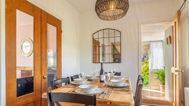 Un coin repas avec une table en bois dressée pour quatre personnes, des chaises, un luminaire suspendu et un miroir au mur.