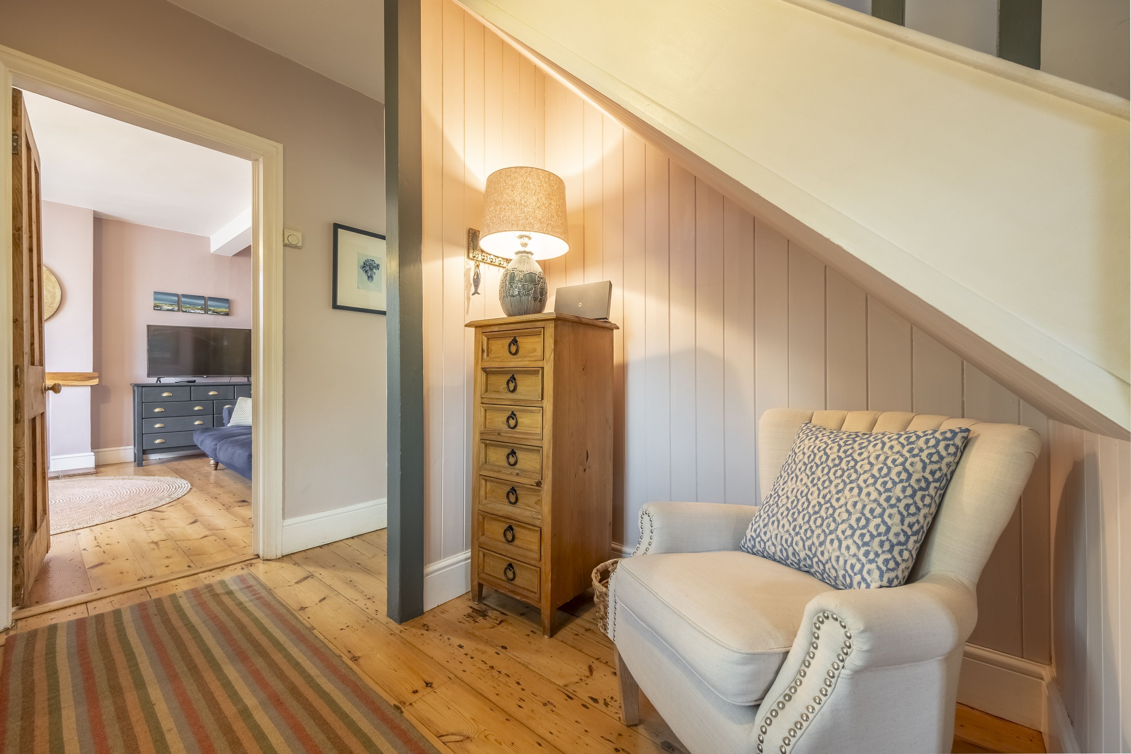 Un salón acogedor con un aparador de madera, una lámpara y un sillón estampado.