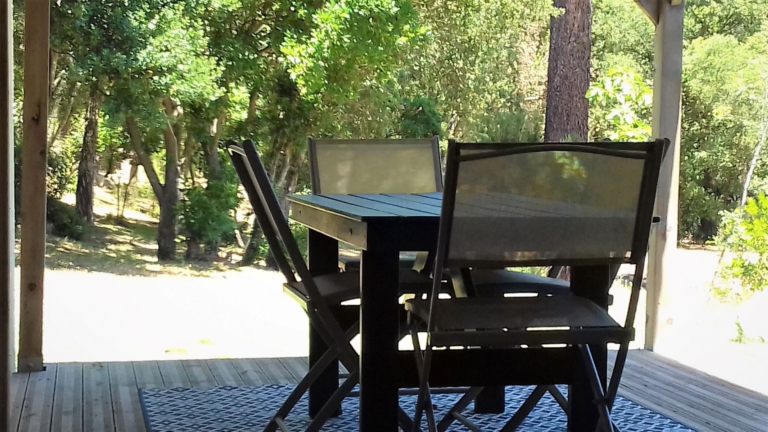 Une terrasse extérieure en bois, avec une table et des chaises, entourée d’arbres.