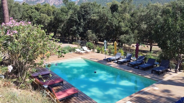 A wooden deck with a swimming pool, lounge chairs, and a view of mountains. - Garden apartment in the heart of nature 10 min from the beach and 5 min from the river (Conca)