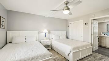 A bedroom with two beds, a ceiling fan, a nightstand with a lamp, and a bathroom visible through an open door.