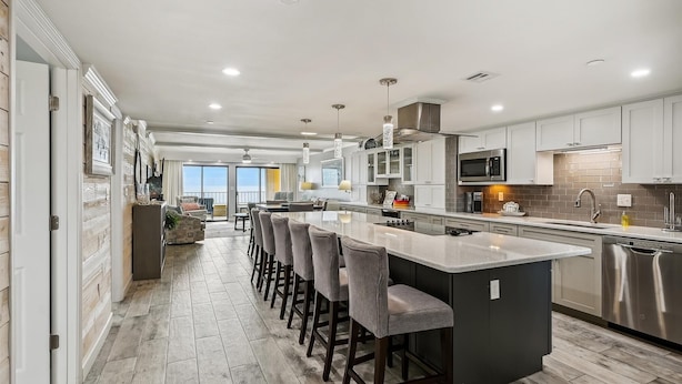 A modern kitchen with a central island, bar stools, stainless steel appliances, and a view to the outside. - Surf Dweller 610 is a Stunning Gulf Front 2 BR - sleep 6 by RedAwning (Fort Walton Beach)